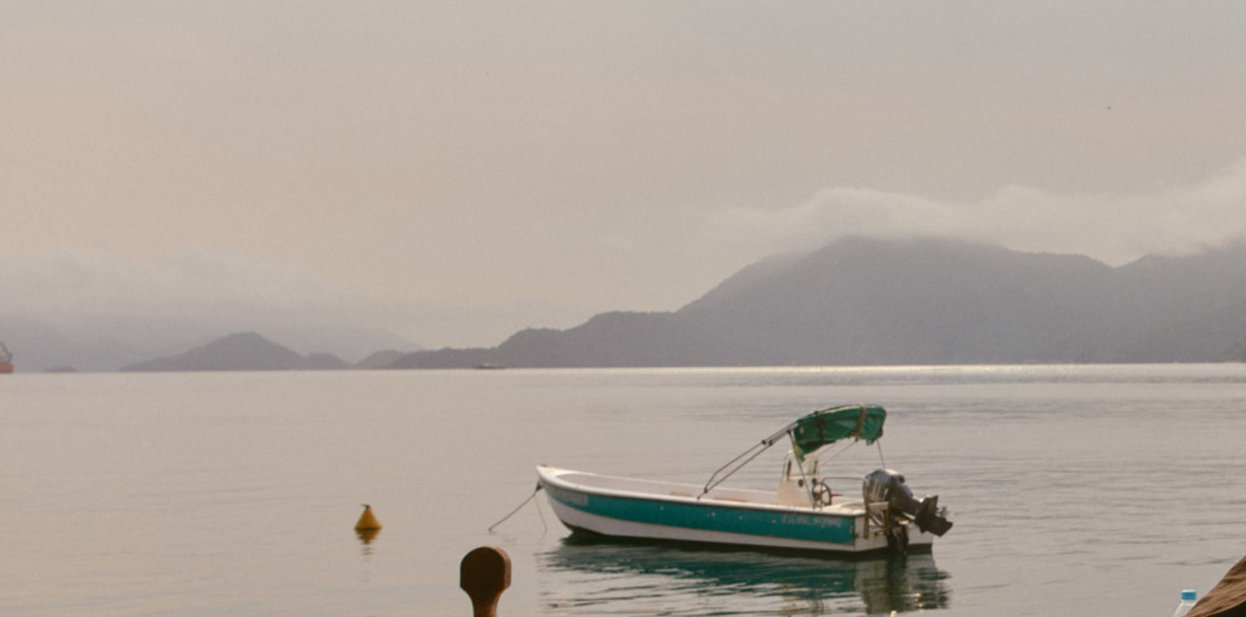 A calm bay at dawn with forested hills and a small boat on still water