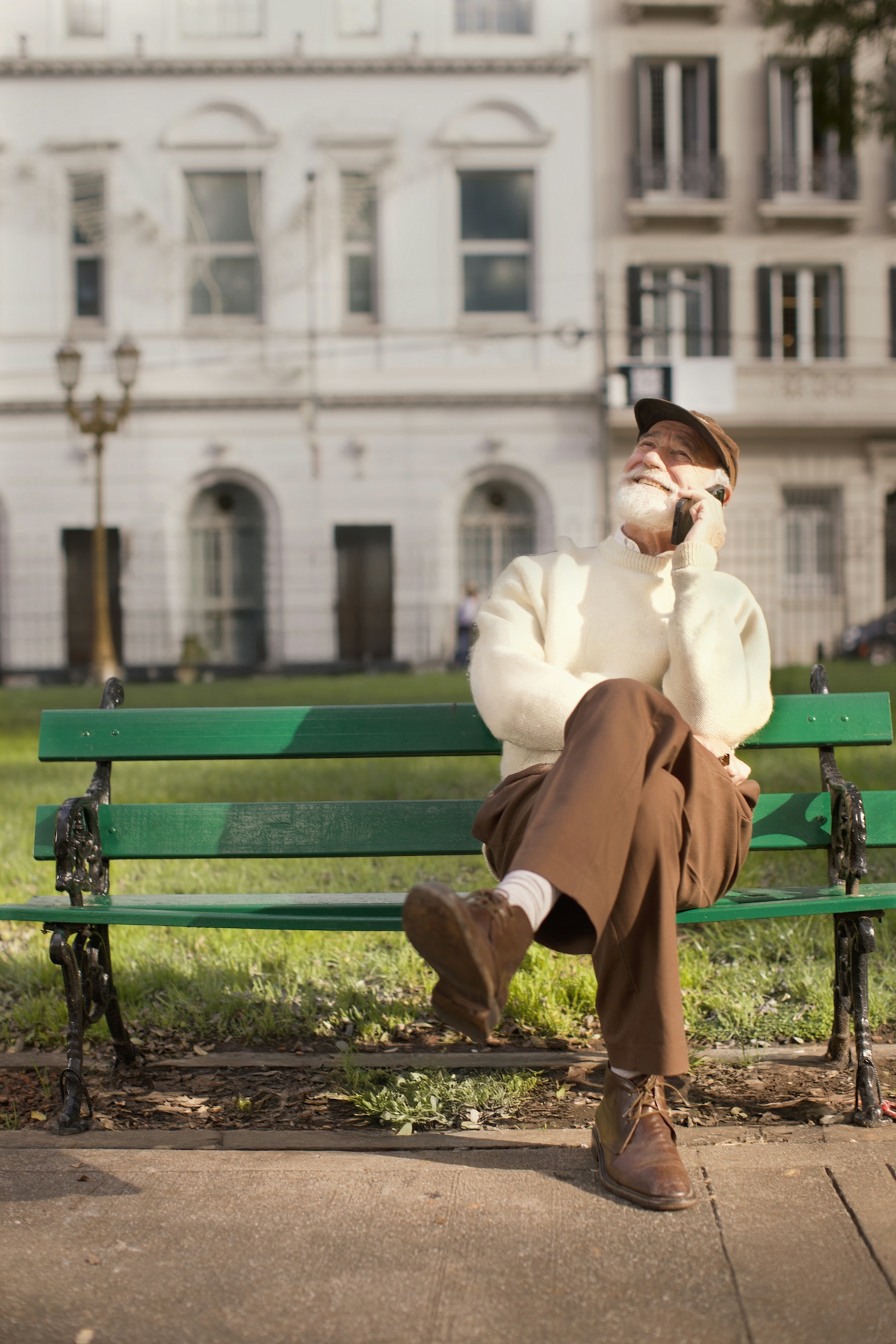 A man sitting on a park bench in warm afternoon light, smiling into a phone call — an everyday outdoor moment of connection.