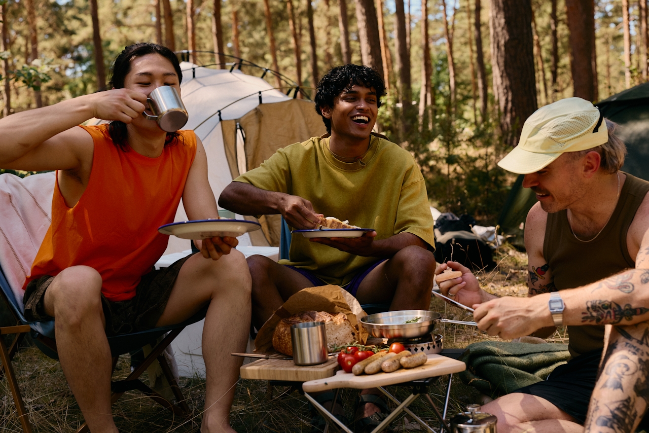 Three friends sharing a meal at a campsite under tall Central Oregon pines — the outdoor life that defines Bend.