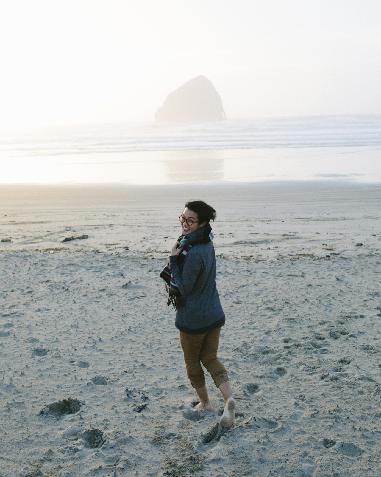 A person walking on an Oregon coast beach at golden hour, with Cape Kiwanda's haystack rock in the distance.