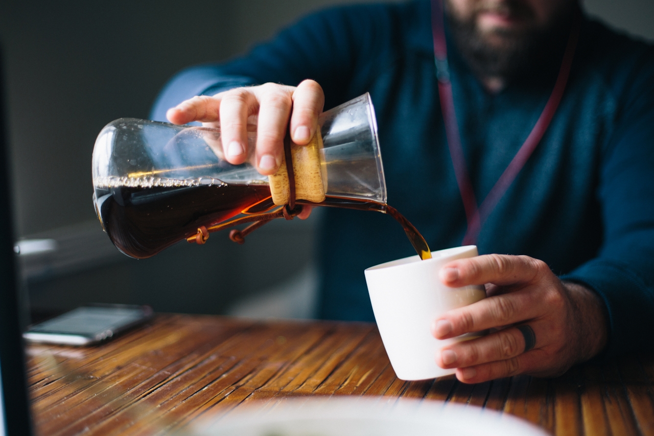 Hands pouring fresh coffee from a Chemex carafe into a white ceramic mug — a steady morning ritual.