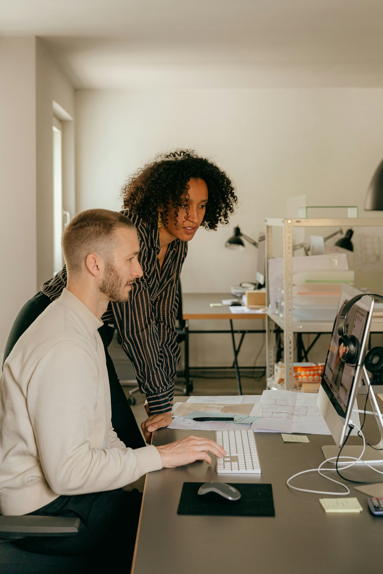 Two coworkers reviewing something together on a desktop monitor in a sunlit office — an everyday moment of professional collaboration.