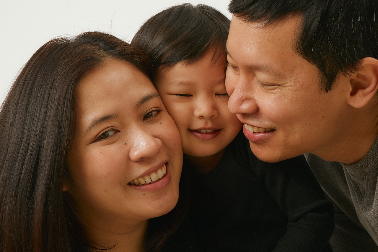 A mother, father, and young child cheek-to-cheek, all smiling — a tender family portrait.